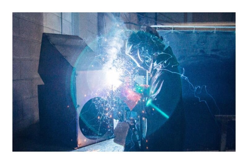 Worker welding grain system parts with protective gear